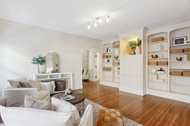 living room with arched walkways, wood finished floors, baseboards, crown molding, and built in features