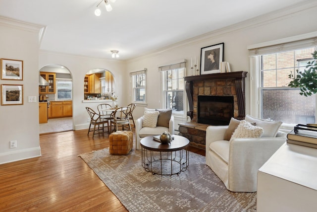 living room featuring arched walkways, healthy amount of natural light, a fireplace, ornamental molding, and wood finished floors