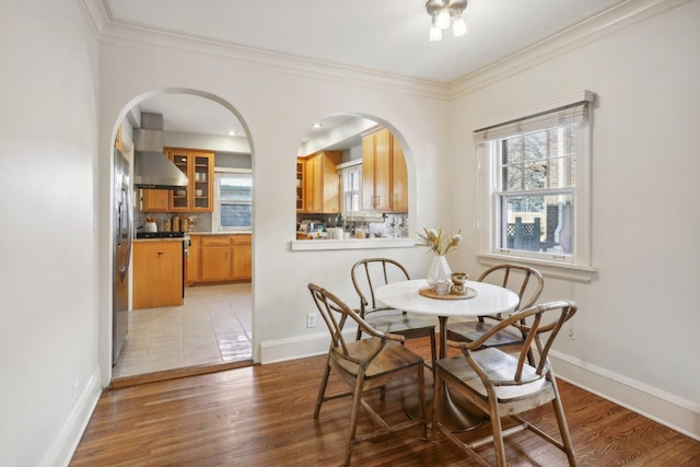 dining room featuring ornamental molding, healthy amount of natural light, light wood-style floors, arched walkways, and baseboards