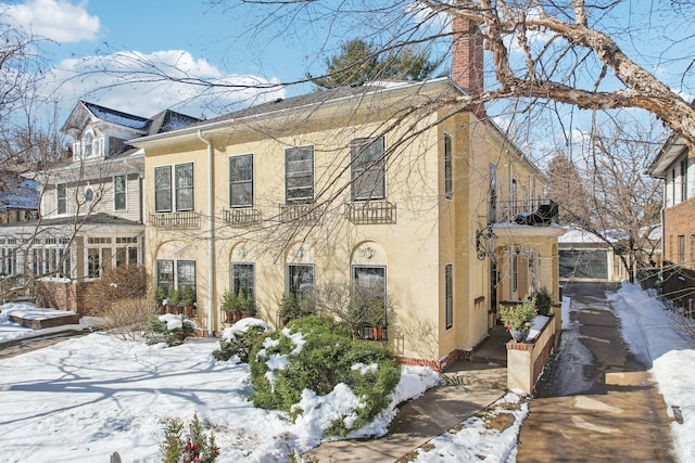 view of snowy exterior with stucco siding and a chimney
