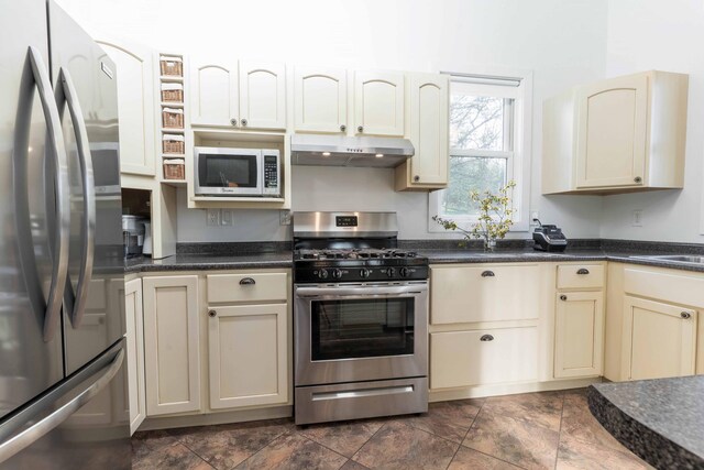 15126 Tumuli Rd, Dalton, MN 56324 - kitchen featuring appliances with stainless steel finishes, cream cabinetry, under cabinet range hood, and dark countertops