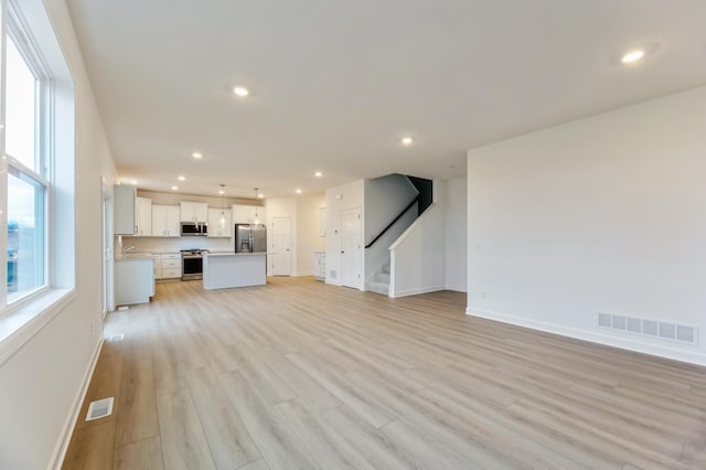 unfurnished living room featuring baseboards, recessed lighting, light wood-style floors, and stairs
