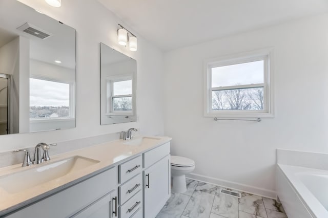 bathroom featuring marble finish floors, a garden tub, toilet, double vanity, and baseboards