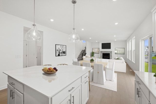 kitchen featuring a fireplace, light wood finished floors, a center island, light countertops, and recessed lighting