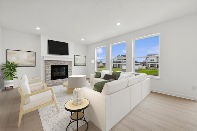 living room featuring a stone fireplace, baseboards, recessed lighting, and light wood finished floors