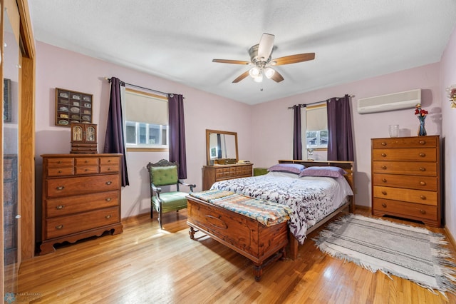 bedroom with a wall mounted AC, light wood finished floors, and a ceiling fan