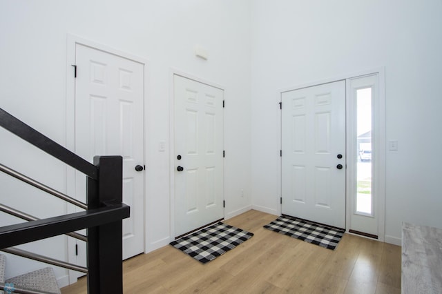 entrance foyer with light wood-style floors, a high ceiling, baseboards, and stairs