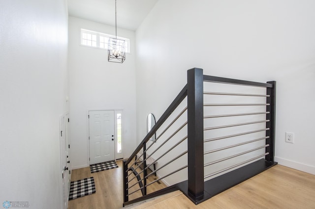 staircase with a chandelier, wood finished floors, a towering ceiling, and baseboards