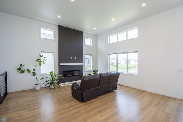 living room with a large fireplace, healthy amount of natural light, recessed lighting, light wood-style floors, and a high ceiling