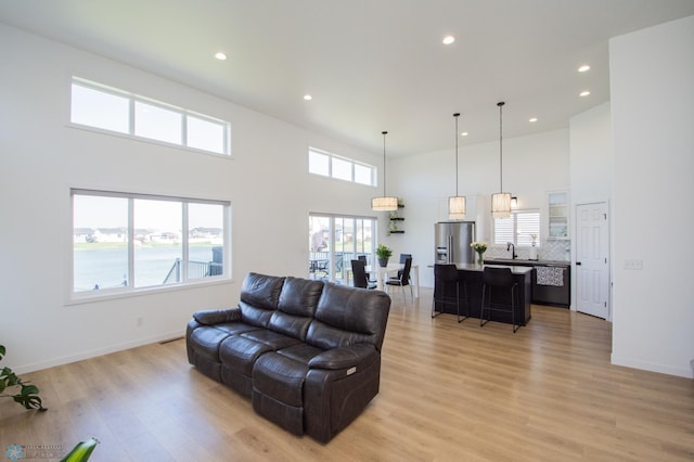 living area with a high ceiling, light wood-type flooring, recessed lighting, and baseboards