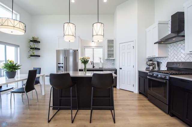 kitchen featuring black range with gas cooktop, wall chimney exhaust hood, stainless steel fridge with ice dispenser, light countertops, and tasteful backsplash