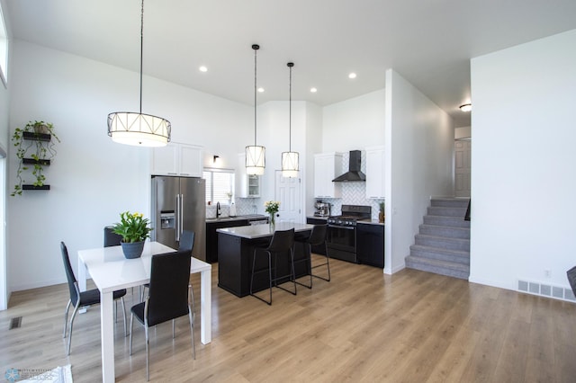 dining area featuring light wood finished floors, recessed lighting, stairs, a towering ceiling, and baseboards