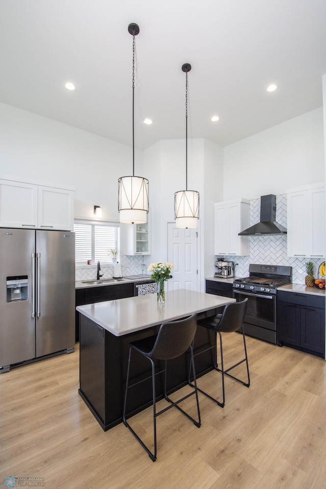 kitchen featuring high end refrigerator, gas range, wall chimney exhaust hood, decorative backsplash, and a breakfast bar area