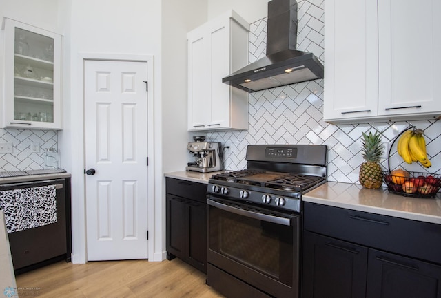 kitchen featuring black gas range, wall chimney exhaust hood, white cabinetry, and backsplash