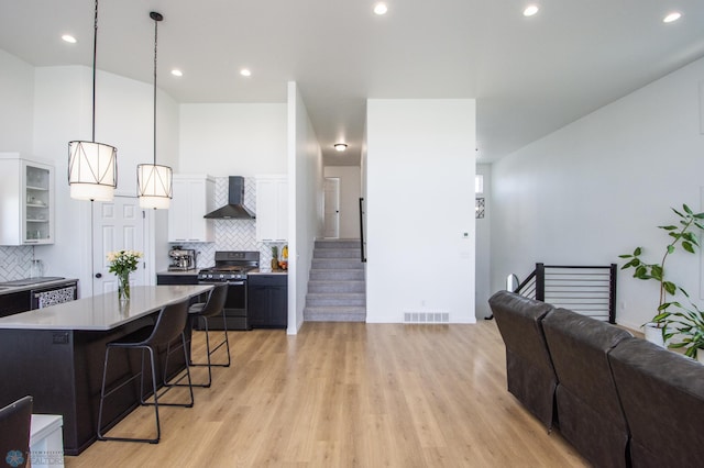 kitchen with stainless steel range with gas stovetop, wall chimney range hood, a kitchen breakfast bar, white cabinetry, and light wood-style floors