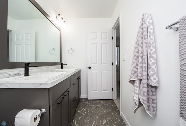 full bath featuring double vanity, baseboards, and marble look tiles