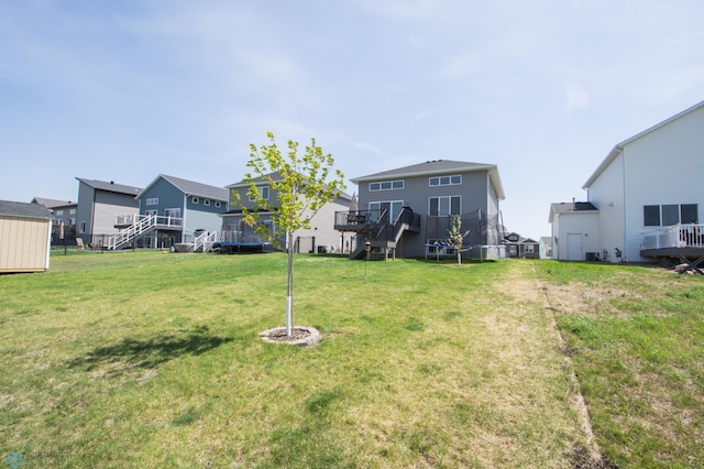 view of green lawn with a trampoline, a residential view, a deck, and stairs