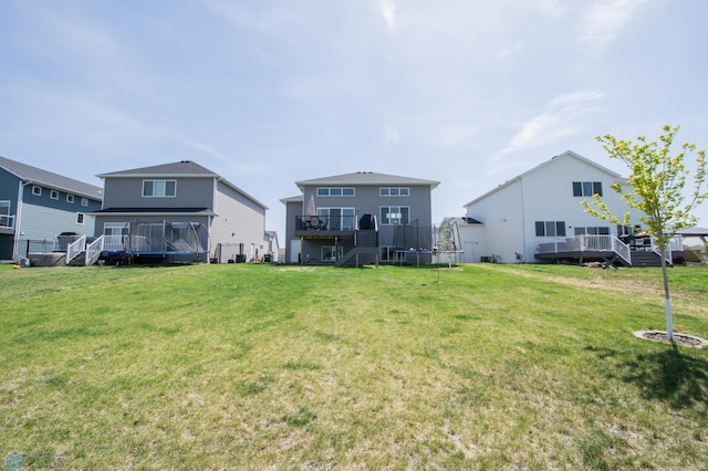 back of property with a trampoline, a wooden deck, stairs, and a yard