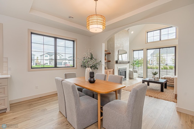 8820 Northern Lights Ave, Fargo, ND 58047 - dining area featuring a large fireplace, light wood-type flooring, arched walkways, baseboards, and a raised ceiling