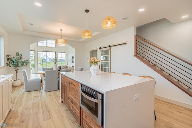 8820 Northern Lights Ave, Fargo, ND 58047 - kitchen with a barn door, a raised ceiling, light wood-style floors, oven, and decorative light fixtures