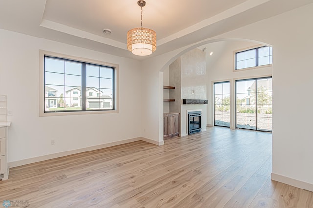 8820 Northern Lights Ave, Fargo, ND 58047 - unfurnished living room featuring a tray ceiling, light wood-type flooring, baseboards, and arched walkways
