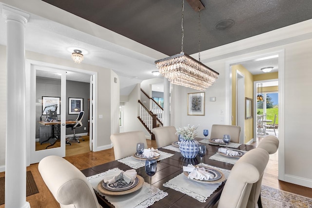 dining space featuring wood finished floors, stairs, a chandelier, baseboards, and ornate columns