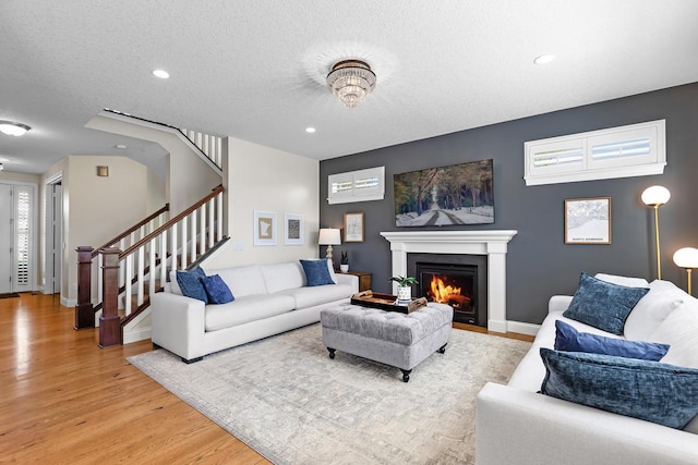 living area with light wood finished floors, stairs, a lit fireplace, recessed lighting, and baseboards