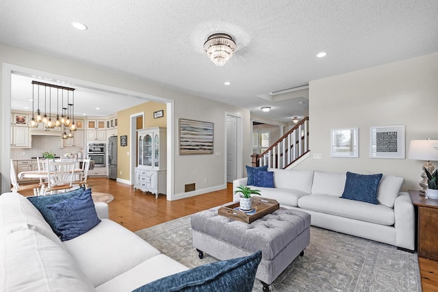 living room with light wood-style flooring, recessed lighting, stairway, a textured ceiling, and baseboards