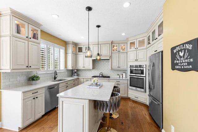 kitchen featuring appliances with stainless steel finishes, a sink, a kitchen island, wood-type flooring, and recessed lighting