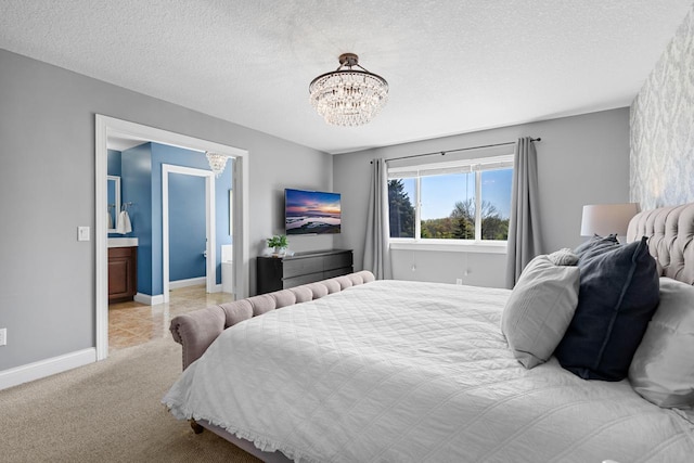 bedroom with a chandelier, baseboards, a textured ceiling, carpet flooring, and ensuite bath