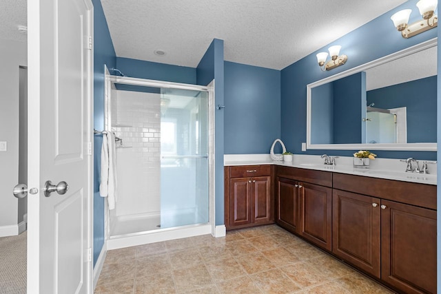 full bath featuring a textured ceiling, a stall shower, double vanity, and baseboards