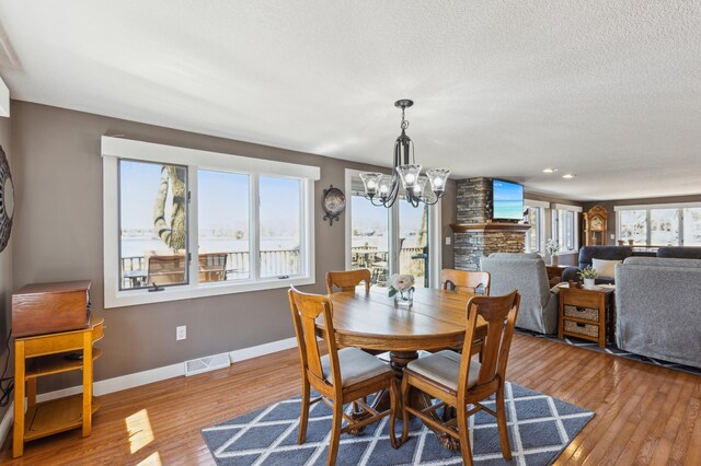 1683 Hansack Ave NE, Saint Michael, MN 55376 - dining room featuring a chandelier, wood-type flooring, baseboards, a stone fireplace, and a textured ceiling
