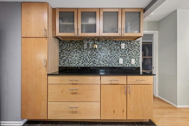 kitchen with baseboards, backsplash, glass insert cabinets, wood finished floors, and dark stone countertops