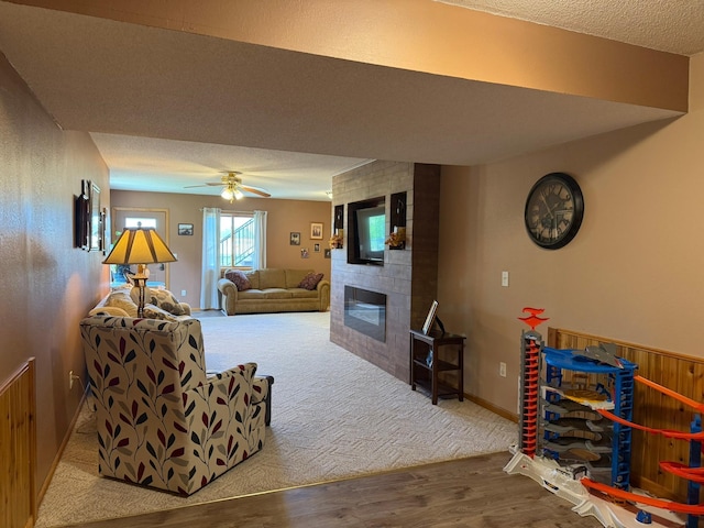 522 Delaware St SW, Lonsdale, MN 55046 - carpeted living room with a tiled fireplace, wood finished floors, a textured ceiling, a ceiling fan, and baseboards