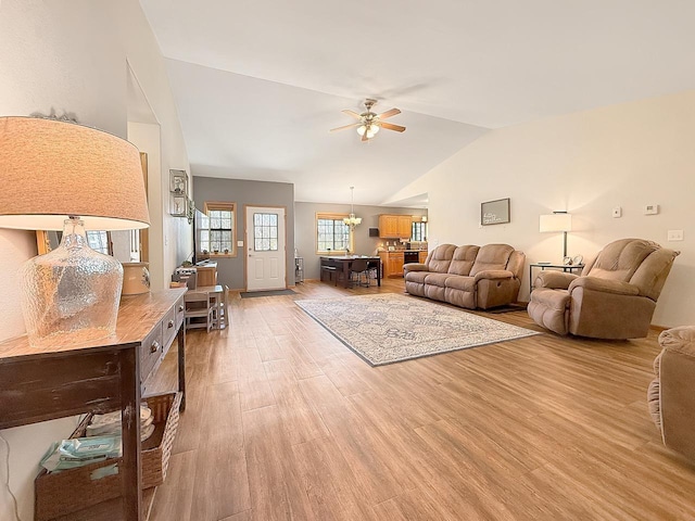 living area with lofted ceiling, ceiling fan, light wood-style floors, and a chandelier