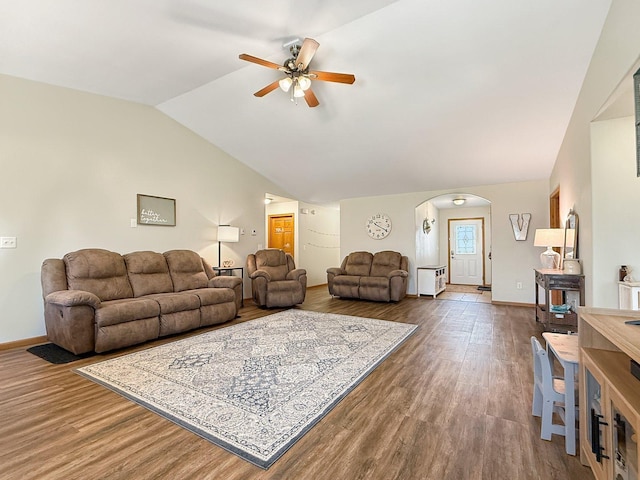 living area featuring ceiling fan, arched walkways, vaulted ceiling, wood finished floors, and baseboards