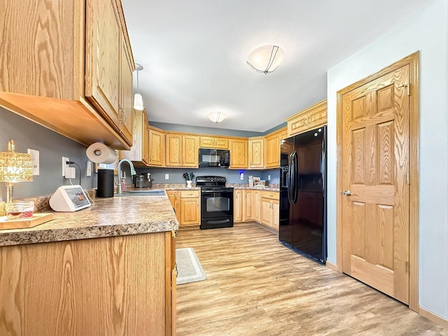 kitchen featuring black appliances, a sink, light wood-style flooring, light countertops, and light brown cabinetry