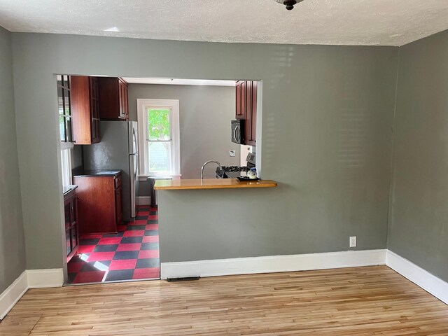 2748 41st Ave S, Minneapolis, MN 55406 - kitchen featuring appliances with stainless steel finishes, baseboards, a textured ceiling, light wood finished floors, and a peninsula