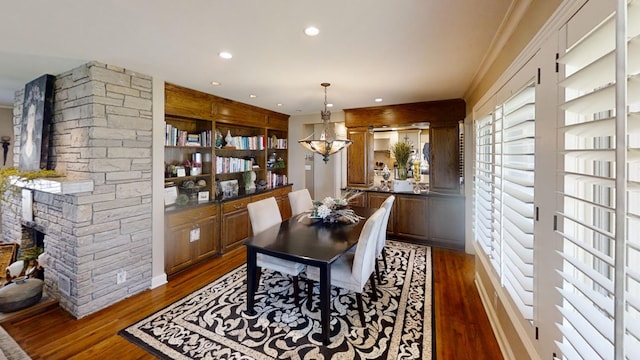 dining space with wood finished floors, a chandelier, recessed lighting, a fireplace, and ornamental molding