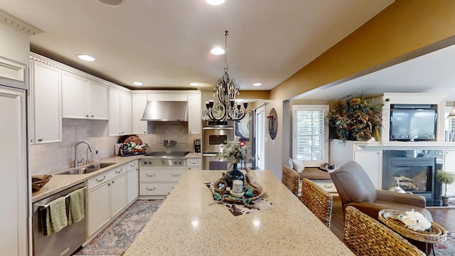 kitchen with a sink, wall chimney exhaust hood, a glass covered fireplace, a chandelier, and stainless steel appliances
