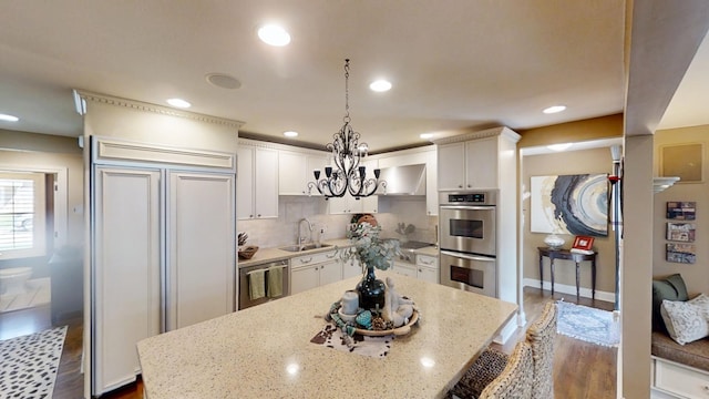 kitchen with a sink, appliances with stainless steel finishes, white cabinets, a kitchen island, and light stone countertops