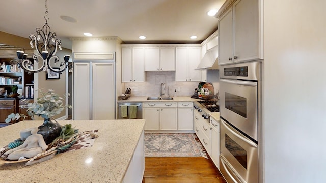 kitchen with a sink, a chandelier, stainless steel appliances, tasteful backsplash, and light stone countertops