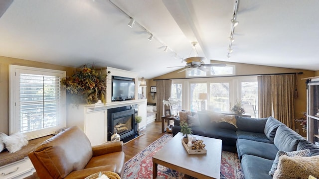 living area with track lighting, a ceiling fan, wood finished floors, a glass covered fireplace, and lofted ceiling