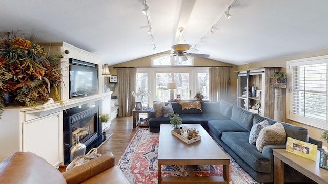 living room featuring track lighting, a ceiling fan, lofted ceiling, wood finished floors, and a glass covered fireplace