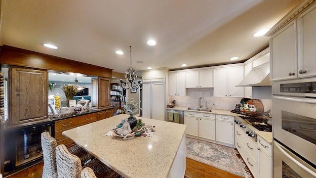 kitchen with stainless steel appliances, wall chimney range hood, a sink, a chandelier, and a center island