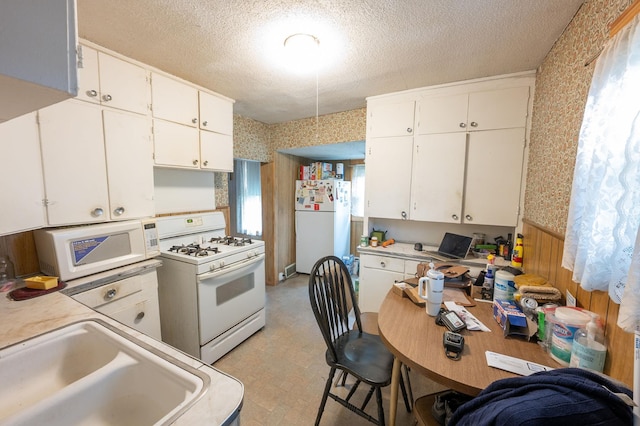 4448 43rd Ave S, Minneapolis, MN 55406 - kitchen with white appliances, wallpapered walls, a sink, white cabinetry, and a textured ceiling