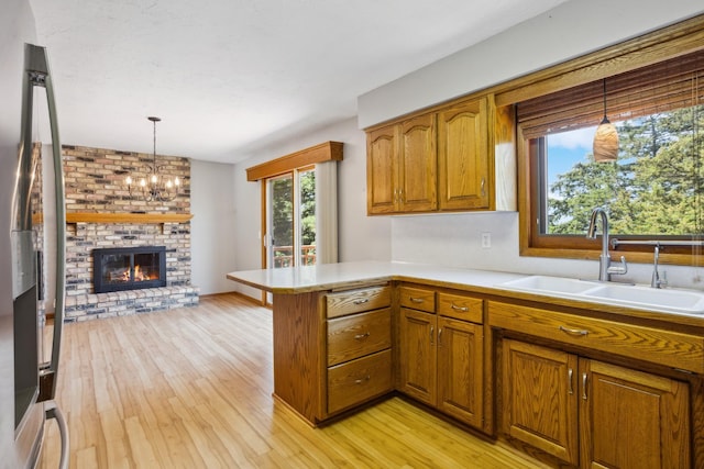 kitchen with a sink, brown cabinets, a peninsula, light wood-style flooring, and light countertops