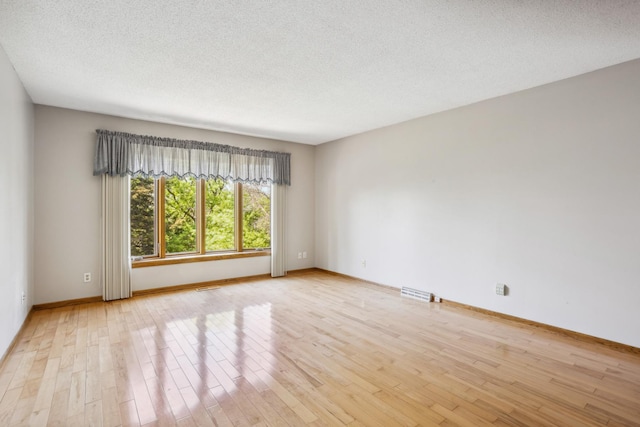 spare room with light wood-style floors, baseboards, and a textured ceiling