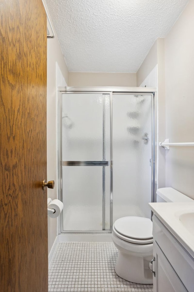 bathroom with a shower stall, a textured ceiling, vanity, tile patterned floors, and toilet