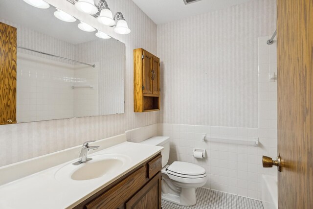 full bath featuring wallpapered walls, tile patterned floors, toilet, vanity, and a wainscoted wall